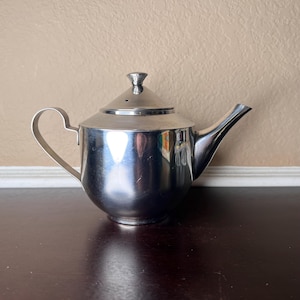 May include: A silver stainless steel teapot with a lid and a curved handle.