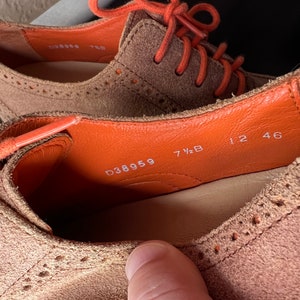 Puede incluir: Primer plano del interior de un zapato de ante marr&oacute;n con cordones naranjas. La talla del zapato es 7 1/2 B y el n&uacute;mero de estilo es D38959. El zapato tambi&eacute;n tiene los n&uacute;meros 12 46 impresos en el interior.