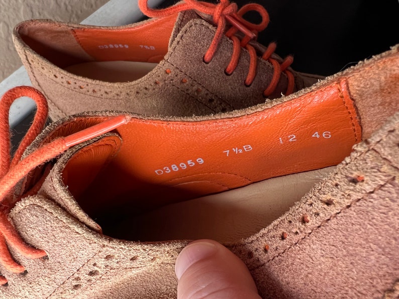 Puede incluir: Primer plano del interior de un zapato de ante marr&oacute;n con cordones naranjas. La talla del zapato es 7 1/2 B y el n&uacute;mero de estilo es D38959. El zapato tambi&eacute;n tiene los n&uacute;meros 12 46 impresos en el interior.