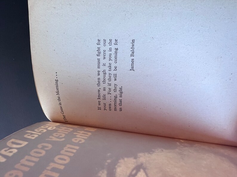 May include: A close-up of a book with a white cover and black text. The text reads "If we know, then we must fight for your life as though it were our own... For if they take you in the morning, they will be coming for us that night." The text is attributed to James Baldwin.