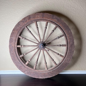 May include: A large, wooden spinning wheel with a circular frame and spokes radiating from the center. The wheel is made of dark brown wood and has a rustic appearance.