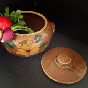 May include: A brown ceramic crock with a lid, decorated with yellow flowers and green leaves. The crock is filled with radishes.