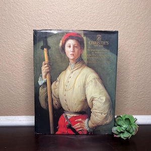 Puede incluir: Un libro de tapa dura con un retrato renacentista de una persona sosteniendo un bastón y una espada. La persona lleva un sombrero rojo, una camisa color crema y pantalones rojos. La portada del libro incluye el texto "Christie's New York".