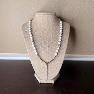 May include: A white and gray marble bead necklace with a gold chain and a gold pendant.