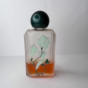 May include: A rectangular glass perfume bottle with vertical ribbed sides and a rounded dark green cap. The clear glass features a painted design of light green flowers with dark green stems and contains an orange liquid at the base.