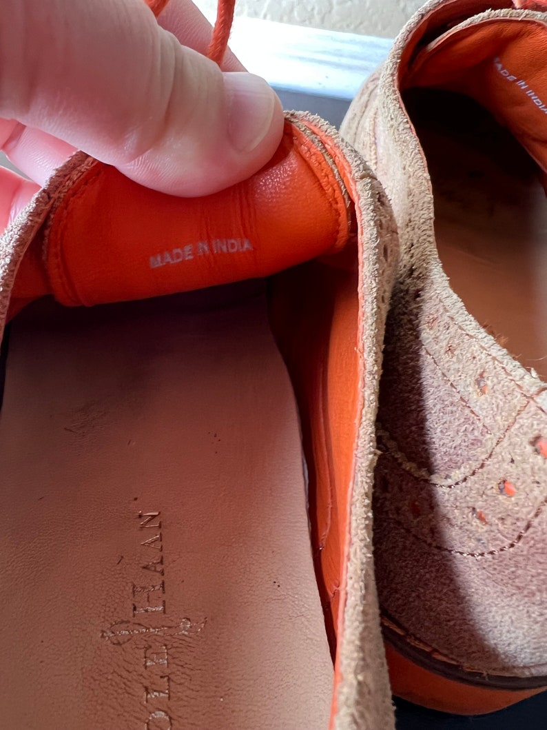Puede incluir: Primer plano del interior de un zapato de ante marr&oacute;n con forro de cuero naranja. El zapato tiene una etiqueta que dice "Hecho en India".