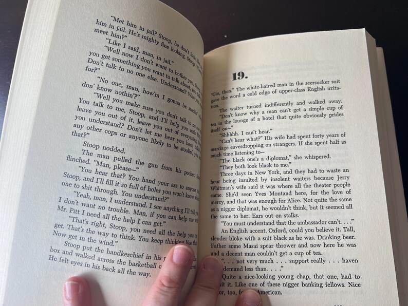May include: Open book with text on the pages. The text is in English and appears to be from a novel. The pages are yellowed, and the book is open to chapter 19. A hand is visible holding the book.