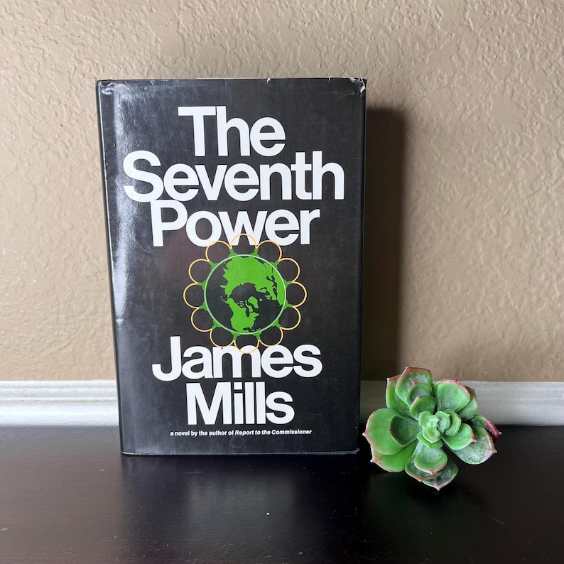 May include: A hardcover book titled "The Seventh Power" by James Mills, with a black cover and white text. The cover features a green and gold graphic of the Earth. A succulent plant is next to the book.