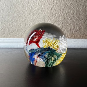 May include: A clear glass paperweight with red, yellow, blue, and white swirling designs inside.