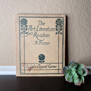Könnte beinhalten: Der Einband eines antiken Buches mit dem Titel "The Art-Literature Readers A Primer" von Eulalie Osgood Grover. Der Einband ist beige mit grünen floralen Mustern und Text.