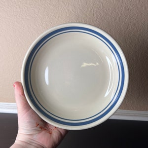 May include: A white ceramic bowl with two blue stripes around the rim.