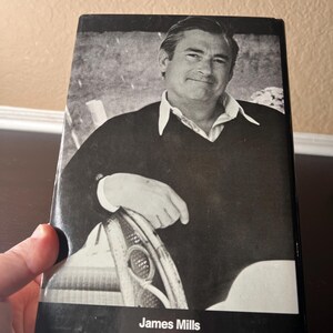 May include: Black and white book cover featuring a portrait of a man in a sweater and collared shirt. The name "James Mills" is printed in white at the bottom. The ISBN and a number are also visible.