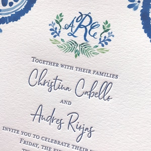 May include: Wedding invitation with a blue and green watercolor floral wreath with the initials "A" and "R" in the center. The text reads "Together with their families Christina Cabello and Andres Rojas invite you to celebrate their..."