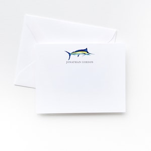 May include: A white stationery card with a blue and yellow marlin illustration and the text "JONATHAN GORDON" printed in blue.