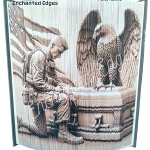 May include: A book sculpture depicting a kneeling soldier, an American flag, and an eagle. The sculpture is in shades of brown and beige, with the text "Pattern by Enchanted Edges" and "Crafted by Polly Hanks".