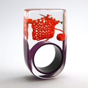 Knitting – extraordinary knitting ring with orange-red knitted wool and knitting needles on a purple ring made of resin