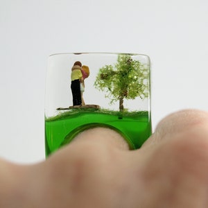 Warm-hearted – paradisiacal lovers ring with kissing mini figures next to a tree and a snake on a green ring made of resin for lovers