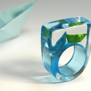 Ship ahoy maritime boat ring with hand-made folded mini boats made of light blue and blue paper on a blue ring made of resin blue/green