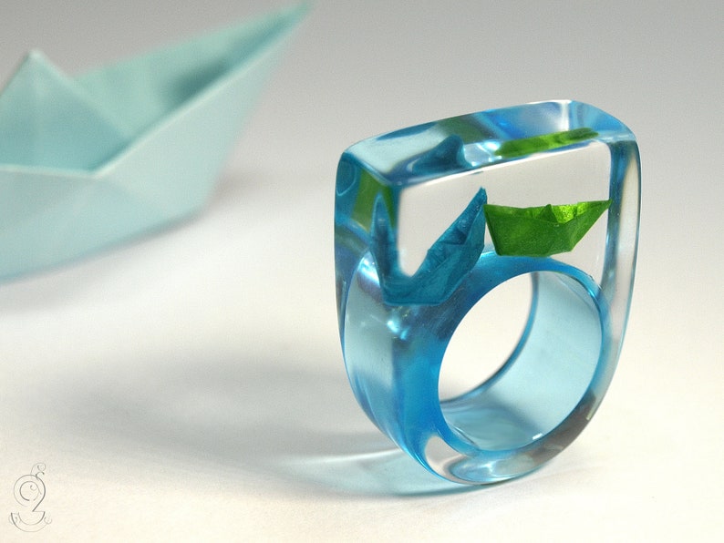 Ship ahoy maritime boat ring with hand-made folded mini boats made of light blue and blue paper on a blue ring made of resin blue/green