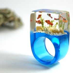 Etsy Design Awards Finalist 2020: Aquarium Fish ring with silver ornamental fish, sand, stones & moss on a blue ring made of resin orange & silver