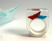 Paper boat ring "Ship ahoy" with hand-made folded mini boats made of red and blue paper on a white ring made of epoxy resin