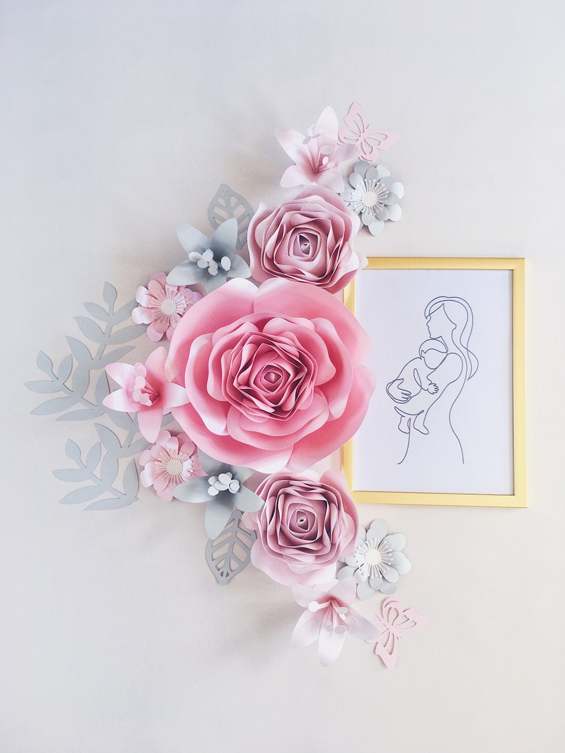 May include: A paper flower arrangement with pink and gray flowers, leaves, and butterflies. A framed line drawing of a mother holding a baby is in the upper right corner.