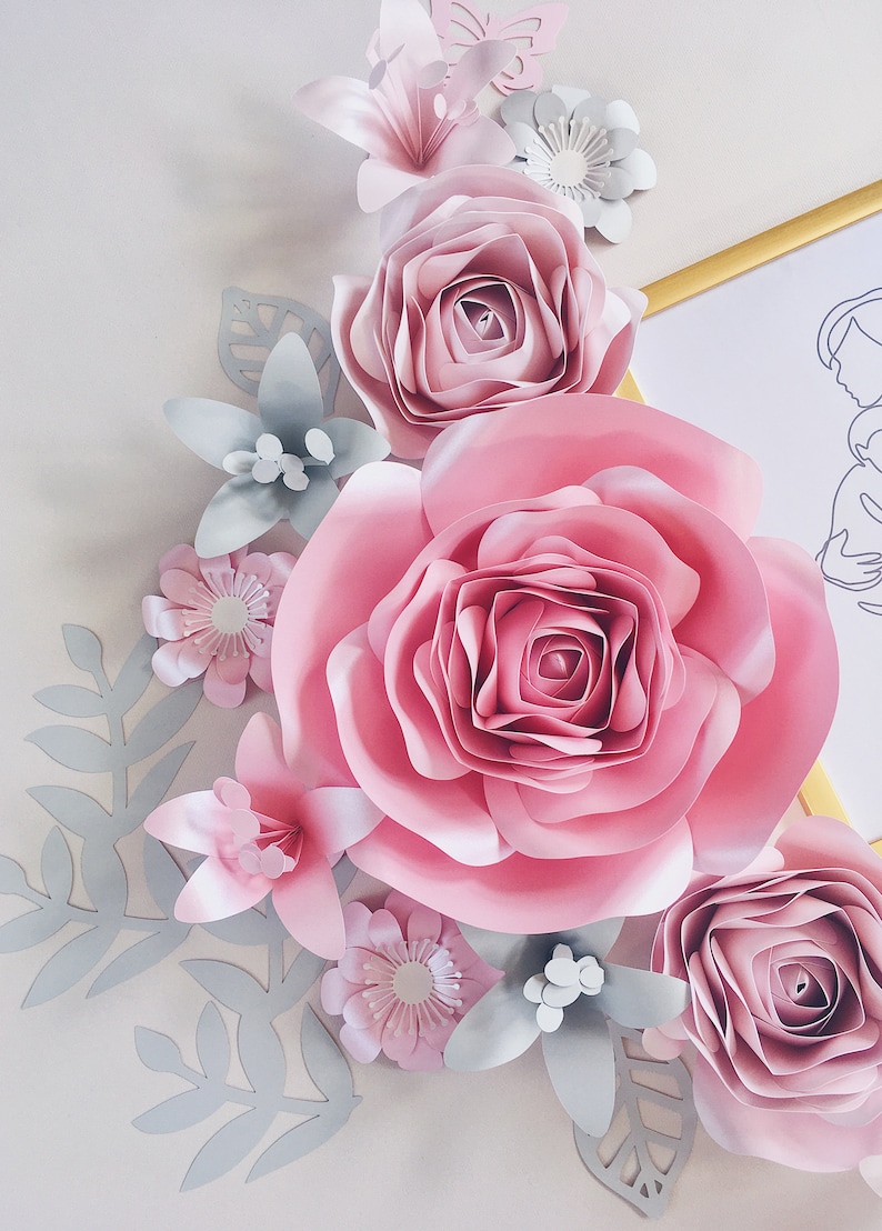 May include: A paper flower arrangement with large pink roses, smaller pink flowers, and gray leaves. The flowers are layered and create a 3D effect.