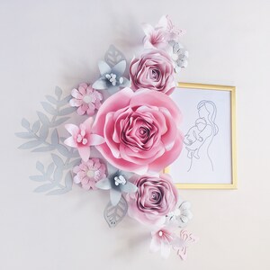 May include: A paper flower arrangement with pink and gray flowers, leaves, and a butterfly. A framed line drawing of a mother holding a child is in the background.