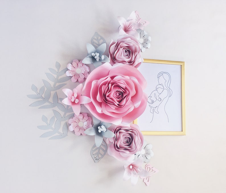 May include: A paper flower arrangement with pink and gray flowers, leaves, and a butterfly. A framed line drawing of a mother holding a child is in the background.