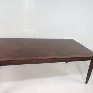 May include: A dark brown wooden dining table with a rectangular top and a geometric pattern in the wood grain. The table has four legs with a simple design.