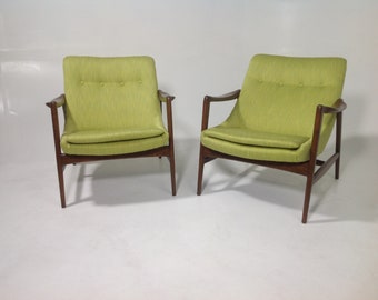 May include: Two green upholstered armchairs with wooden frames. The chairs have a mid-century modern design.