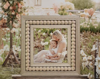 May include: A square, light-colored wooden picture frame with a beaded border. The frame surrounds a photograph of a mother and child embracing in a garden setting. The background features flowers and soft lighting.