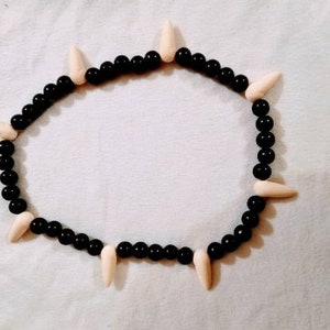 May include: A black and white beaded necklace with white pointed beads. The necklace is made of small black beads and larger white beads that are pointed at the top.