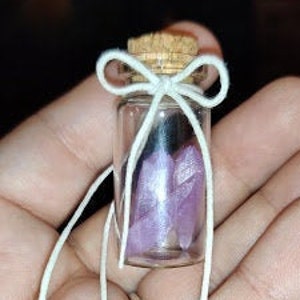 May include: A small glass bottle with a cork stopper tied with a white ribbon bow. The bottle contains small purple crystals.