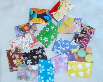 May include: A collection of small, rectangular paper envelopes featuring a variety of colorful patterns, including floral designs, cherry blossoms, geometric shapes, polka dots, and solid yellow with white hearts, scattered across a plain surface.