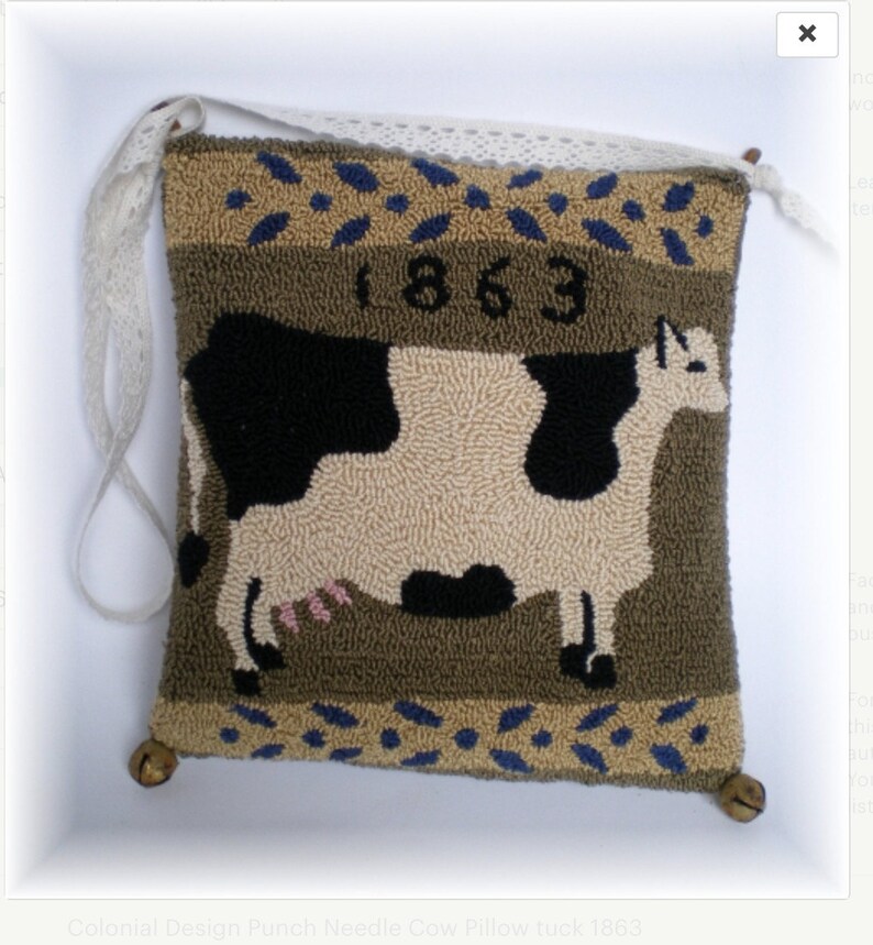 May include: A brown and green pillow with a black and white cow design. The pillow has a white lace trim and two bells on the bottom corners. The year 1863 is embroidered on the pillow.