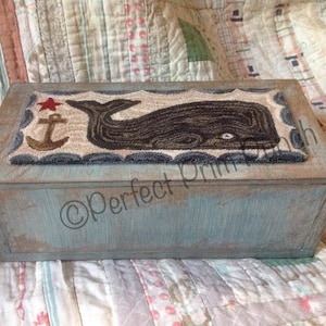May include: A rectangular wooden box with a light blue painted finish. The lid features a rug design with a whale, anchor, and star. The box has a nautical theme and is likely used for storage.