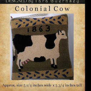 May include: A brown and tan pillow with a black and white cow design. The pillow has a green background and the year 1863 is printed on the top. The pillow is approximately 5 1/4 inches wide and 5 3/4 inches tall.