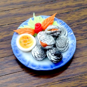 May include: A blue and white plate with a serving of steamed clams, a small bowl of dipping sauce, and a garnish of green lettuce and orange carrots.