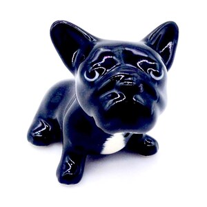 以下が含まれることがあります： 座っているフレンチブルドッグの光沢のある黒いセラミックフィギュア。犬は胸に白い斑点があり、大きな耳や表情豊かな目など、顔の特徴が詳細に表現されています。白い背景に配置されています。
