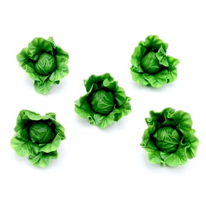 Könnte beinhalten: Fünf Miniatur-Skulpturen von grünen Kohlköpfen mit detaillierten Blattstrukturen auf weißem Hintergrund. Die Kohlköpfe sind leuchtend grün, und die Blätter sind aufwendig geformt, um echten Kohlköpfen zu ähneln.