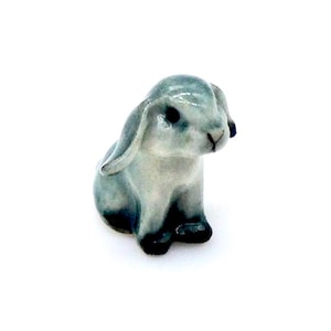 Op de afbeelding: Een klein, grijs keramiek konijnenbeeldje met zwarte ogen en een witte neus. Het konijn zit met zijn oren omhoog.