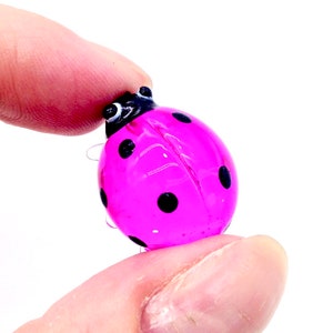 May include: A small pink glass ladybug with black spots. The ladybug is about the size of a dime.