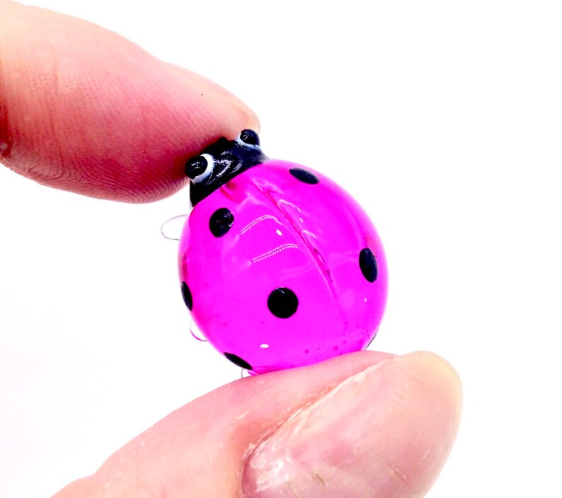 May include: A small pink glass ladybug with black spots. The ladybug is about the size of a dime.