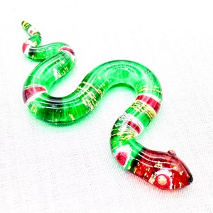 May include: A green glass snake with red and gold accents. The snake is curled in an 'S' shape.