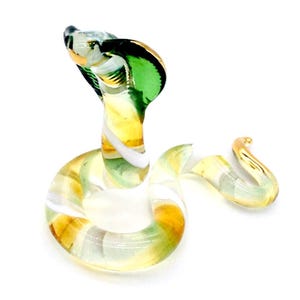 May include: A glass figurine of a green and white snake with a raised head. The snake is coiled and has a gold-colored tail.