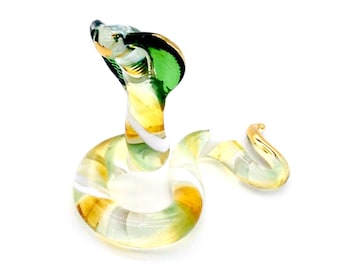 May include: A glass figurine of a green and white snake with a raised head. The snake is coiled and has a gold-coloured tail.