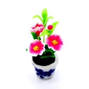 May include: A miniature ceramic flower pot with a blue floral design. The pot contains a small arrangement of pink and white flowers with yellow centers, green leaves, and a red berry.