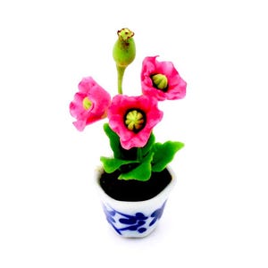 Könnte beinhalten: Eine Miniatur-Blumenarrangement mit rosa Blüten in einem blau-weißen Keramiktopf. Die Blumen sind aus Ton und haben grüne Blätter.