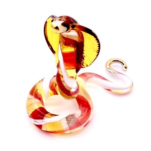 May include: A glass figurine of a cobra with a red, white, and yellow striped body. The cobra is in a coiled position with its head raised and its hood expanded.